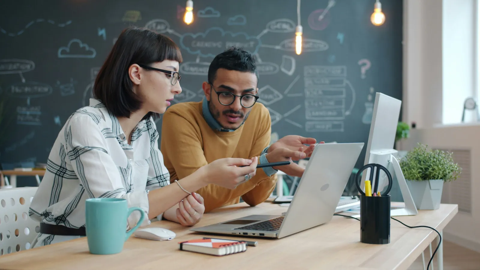 Two colleagues at a desk working through a problem together over a laptop